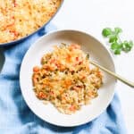 bowl of crawfish casserole with a gold fork on a blue napkin next to fresh parsley and a pot of casserole.