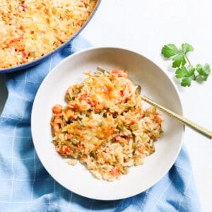 bowl of crawfish casserole with a gold fork on a blue napkin next to fresh parsley and a pot of casserole.