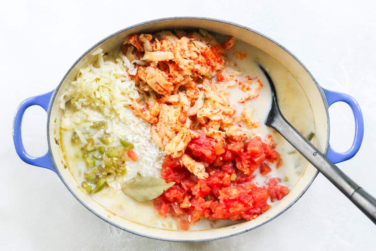 blue pot with crawfish tails, cheese, bay leaf, veggies, rotel tomatoes, rice, water, and milk before being stirred together.