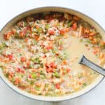 crawfish stirred into a pot with veggies, rice, milk, and broth being stirring with a black spoon.