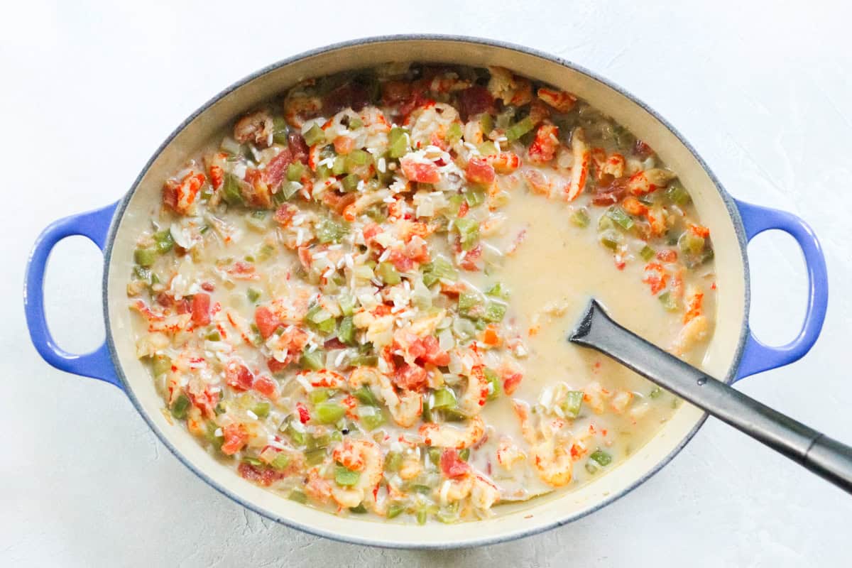 crawfish stirred into a pot with veggies, rice, milk, and broth being stirring with a black spoon.