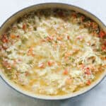 crawfish casserole in a blue pot covered in cheese before baking.
