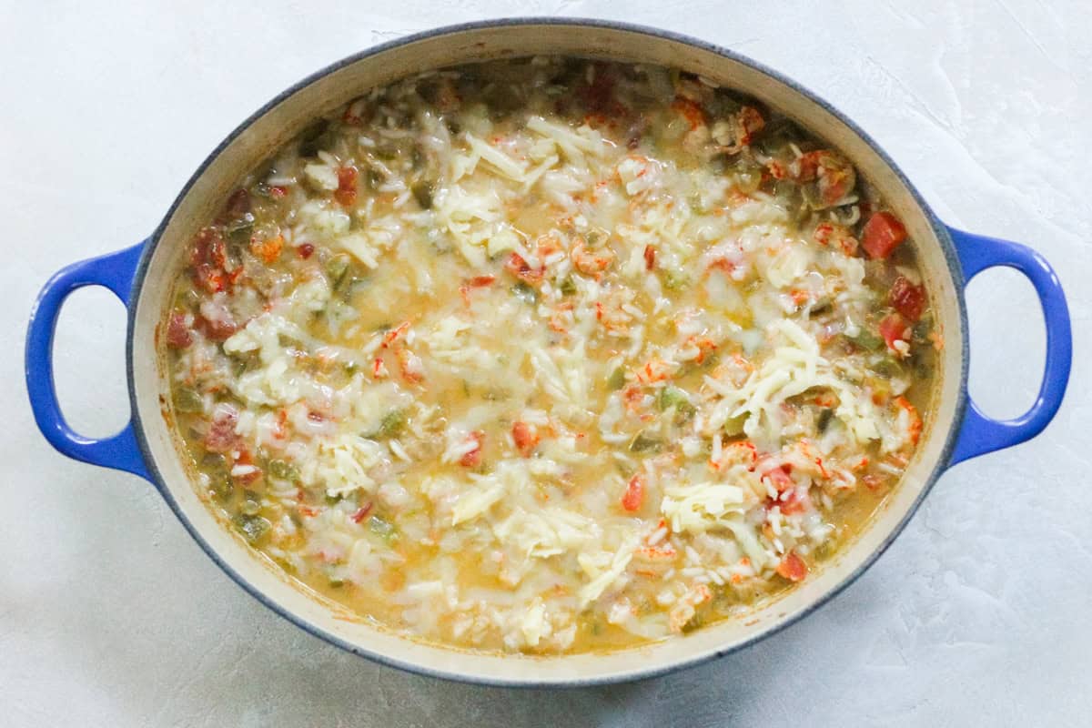 crawfish casserole in a blue pot covered in cheese before baking.