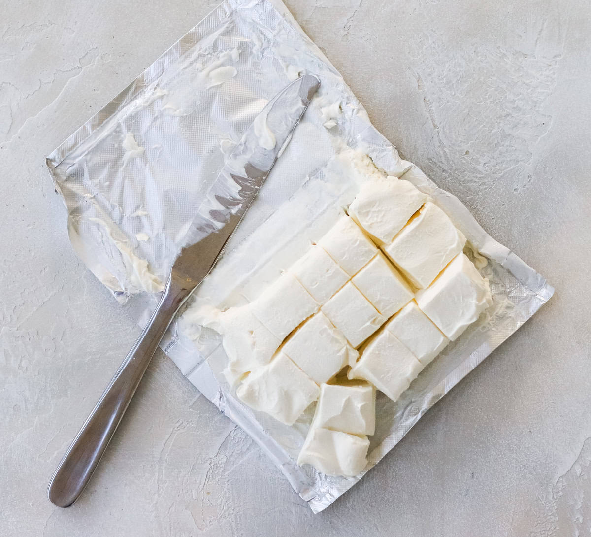 chopped cream cheese in foil wrapper with a silver butter knife.
