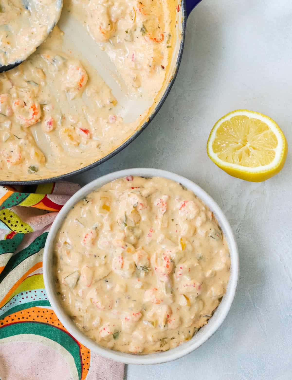 bowl of crawfish dip next to a blue pan with extra dip next to a colorful napkin and fresh lemon.