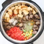 instant pot filled with diced tomatoes, spices, mixed veggies, beef chunks, and potatoes.