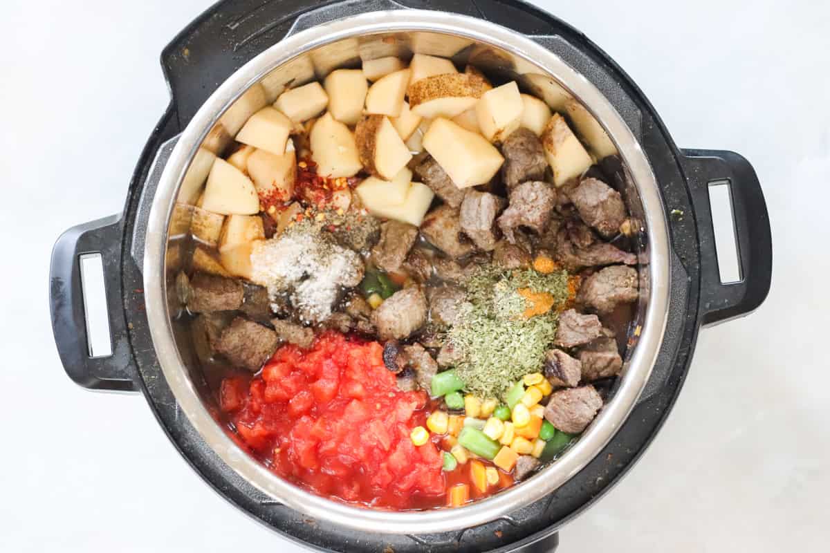 instant pot filled with diced tomatoes, spices, mixed veggies, beef chunks, and potatoes.