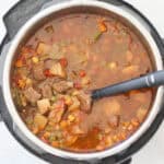 instant pot filled with vegetable beef soup after cooking being stirred with a black spoon.