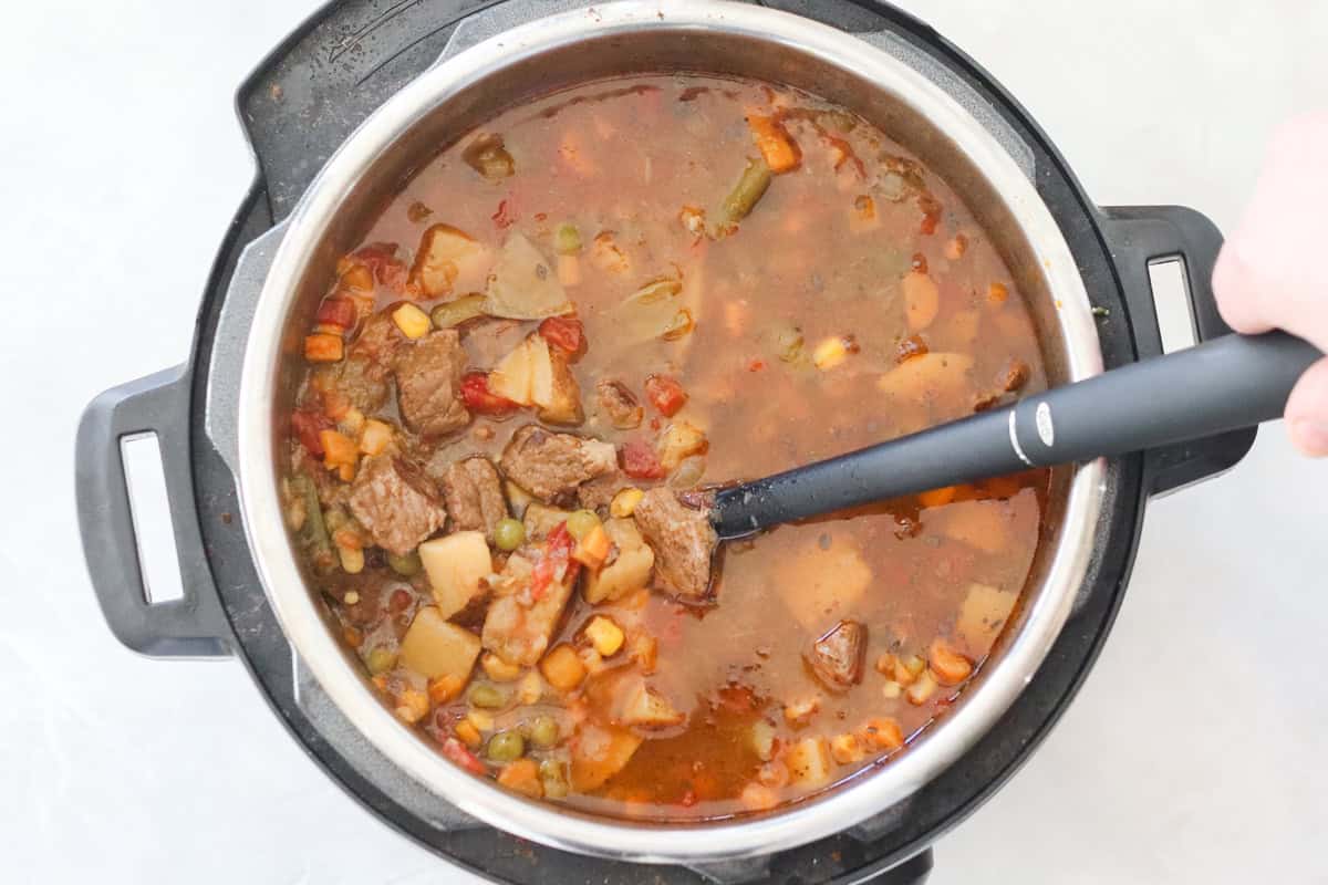 instant pot filled with vegetable beef soup after cooking being stirred with a black spoon.