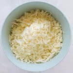 blue mixing bowl full of shredded white cheddar cheese.