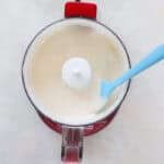 red mini food processor with blended cottage cheese and a blue spatula.