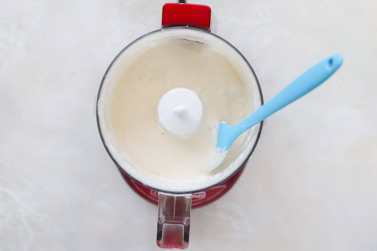 red mini food processor with blended cottage cheese and a blue spatula.