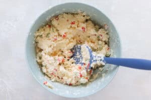 blue mixing bowl with cottage cheese and blue spatula.