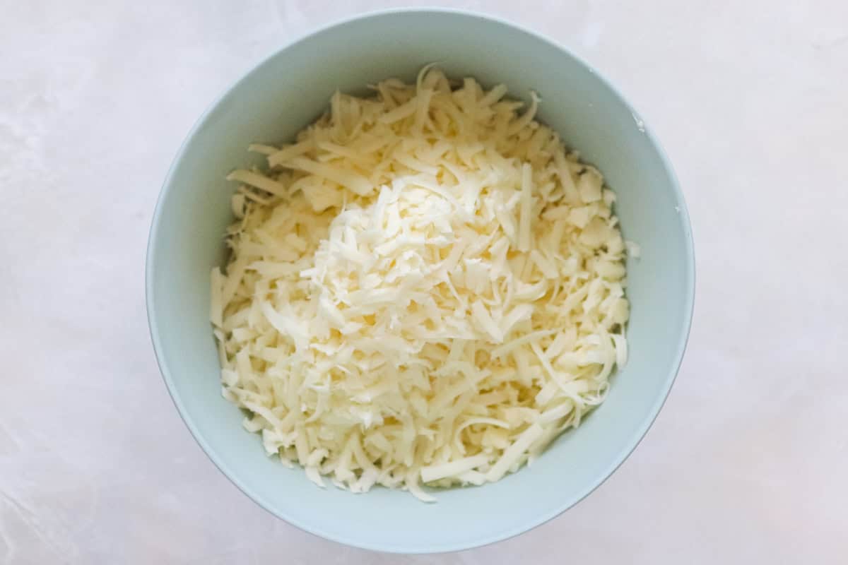blue mixing bowl full of shredded white cheddar cheese.