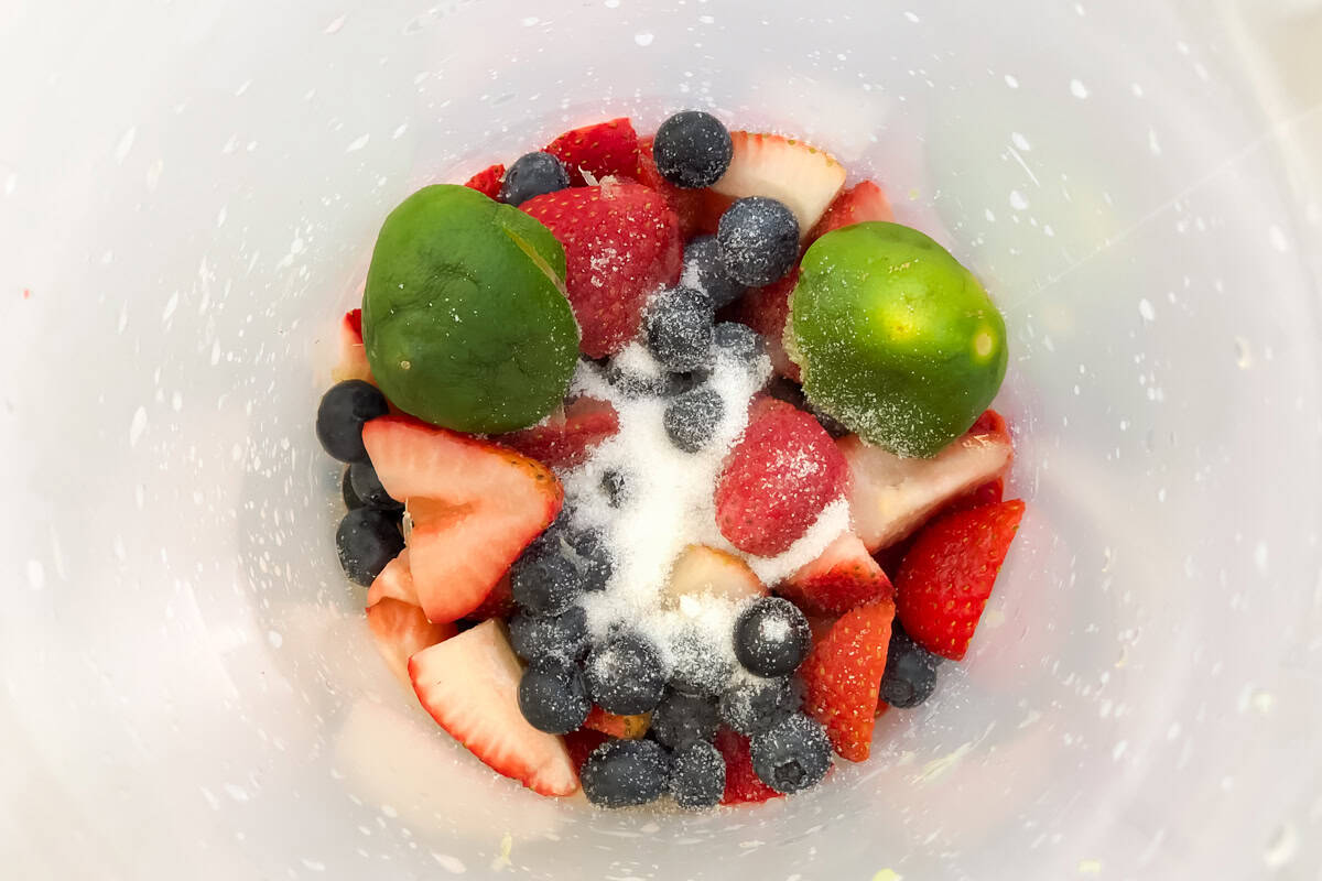 sliced strawberries, blueberries, and lime in a pitcher sprinkled with granulated sugar.