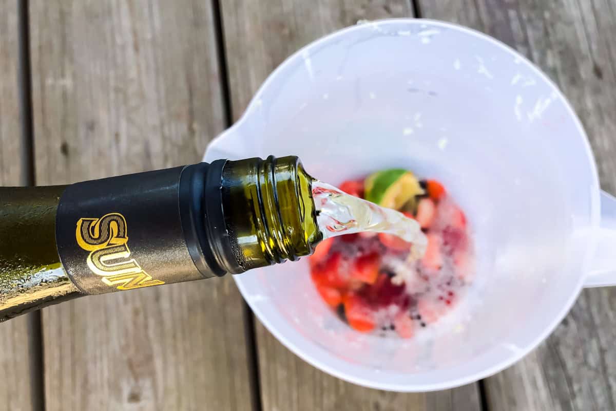 white wine being poured into a pitcher with fresh fruit.