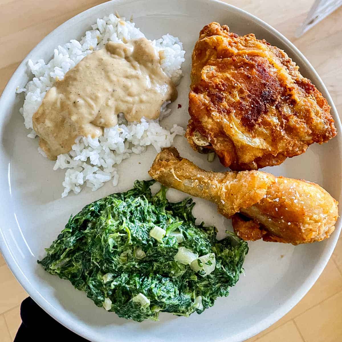plate with fried chicken, creamed spinach, and rice and gravy.