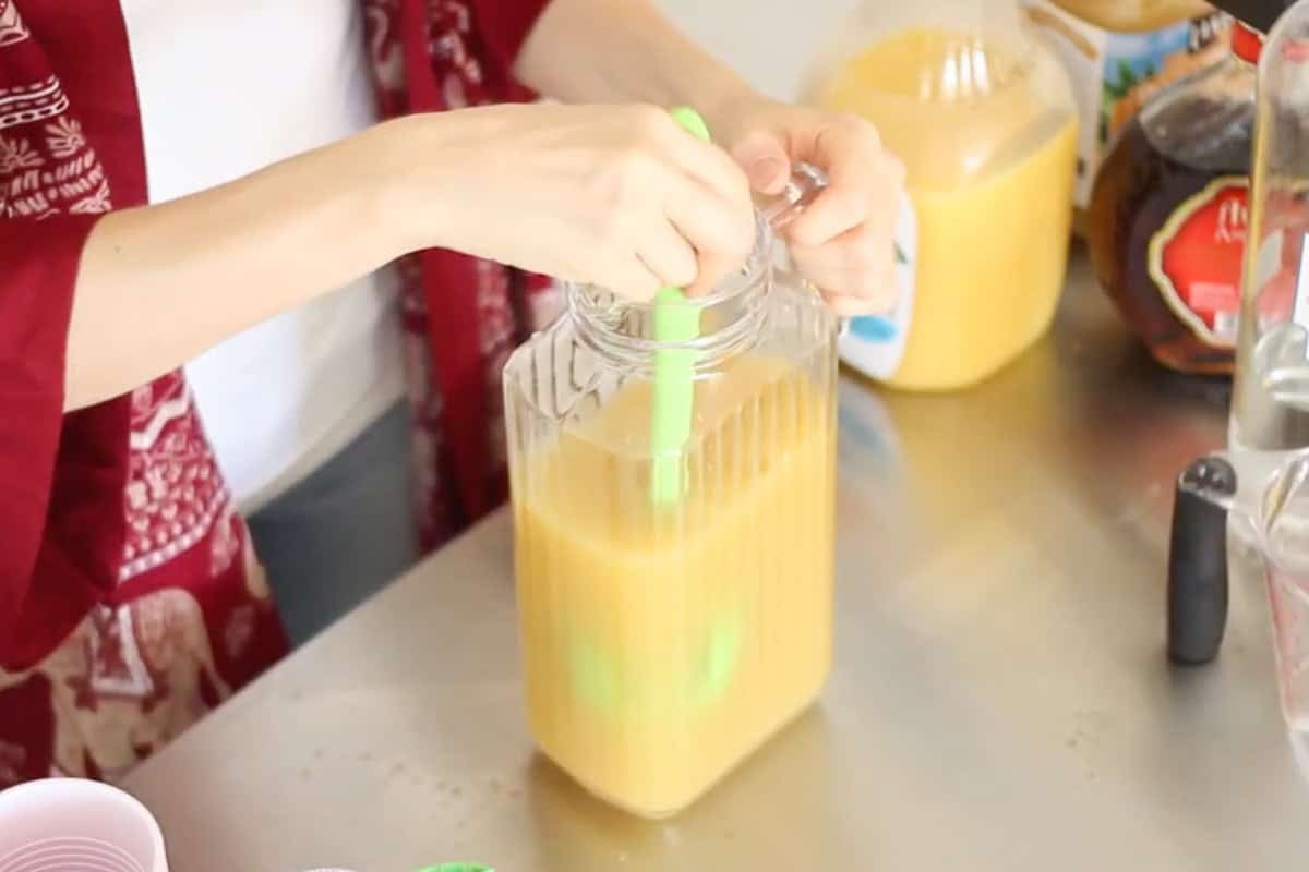 hand stirring together a pitcher with a yellow hammer drink.