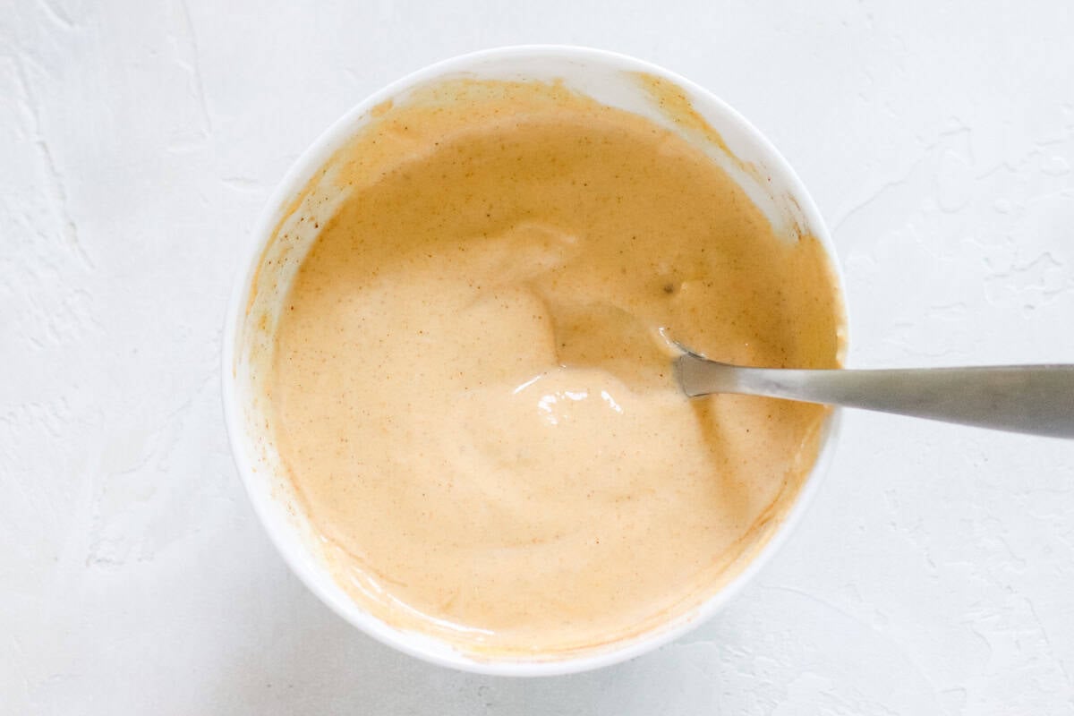 silver spoon in a white bowl of pumpkin yogurt.
