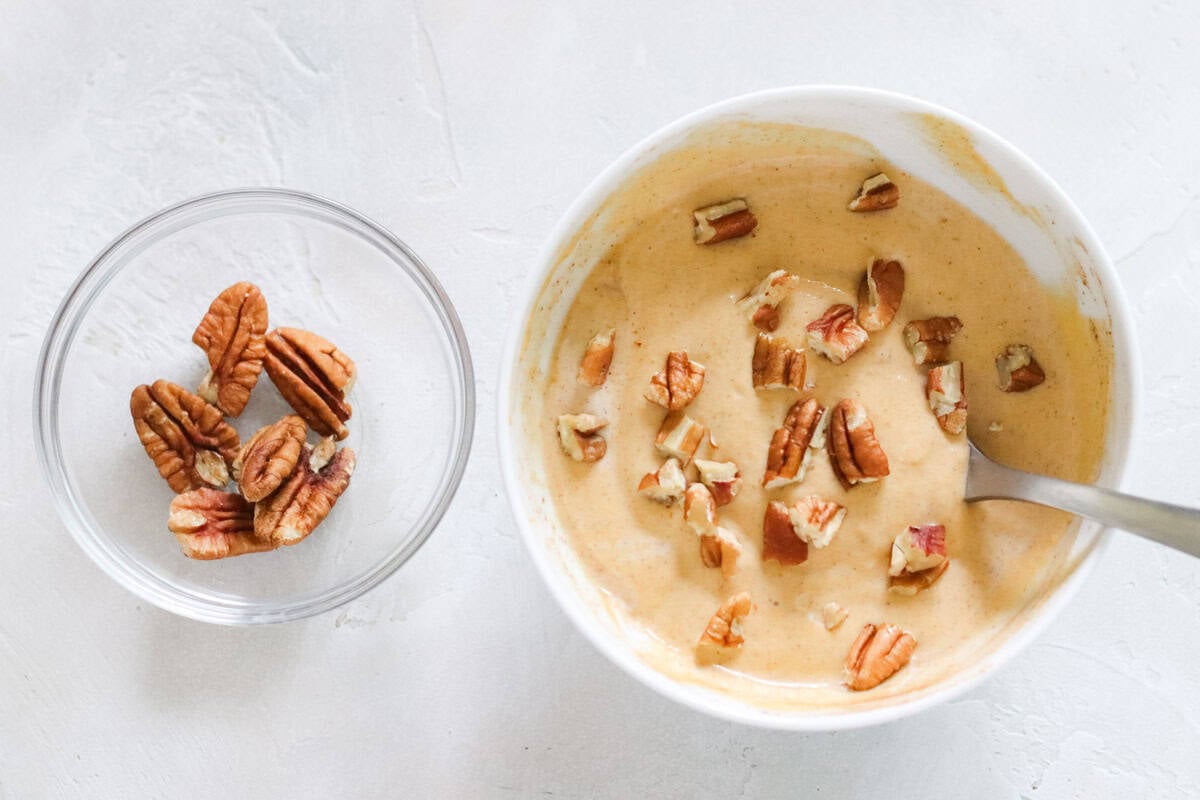 clear bowl of pecan halves next to a white bowl of pecan topped pumpkin yogurt.
