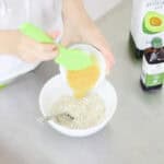 hand pushing apple sauce into a bowl of microwave oatmeal cookie dry ingredients with a green spatula.