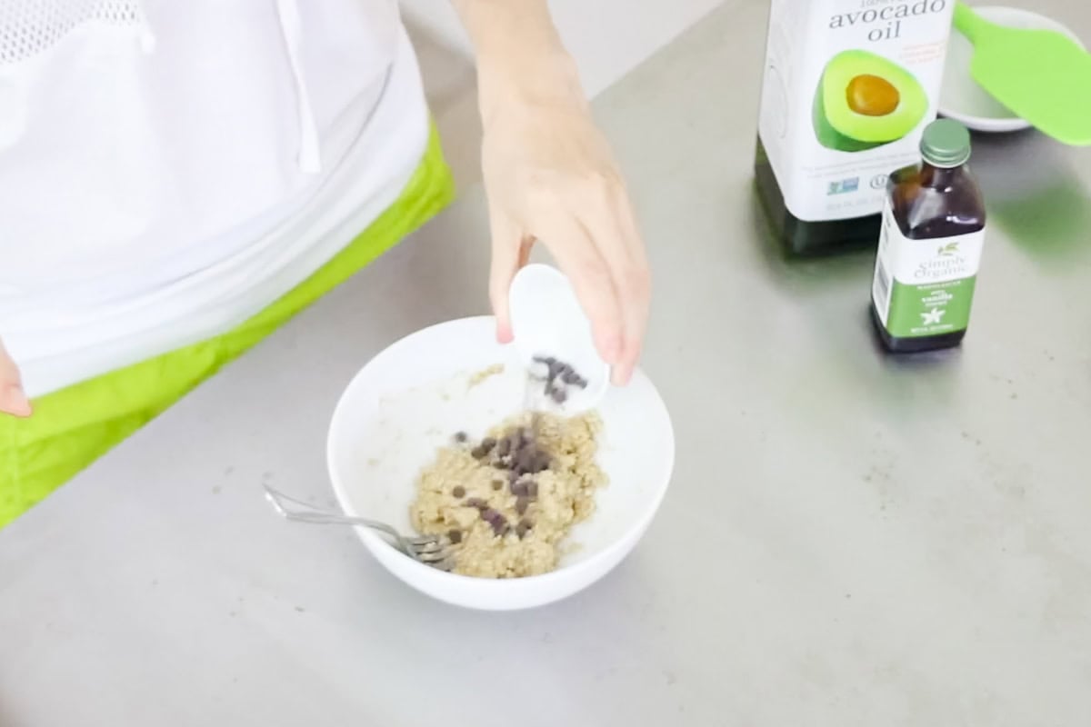 hand pouring mini chocolate chips into a bowl of cookie dough.