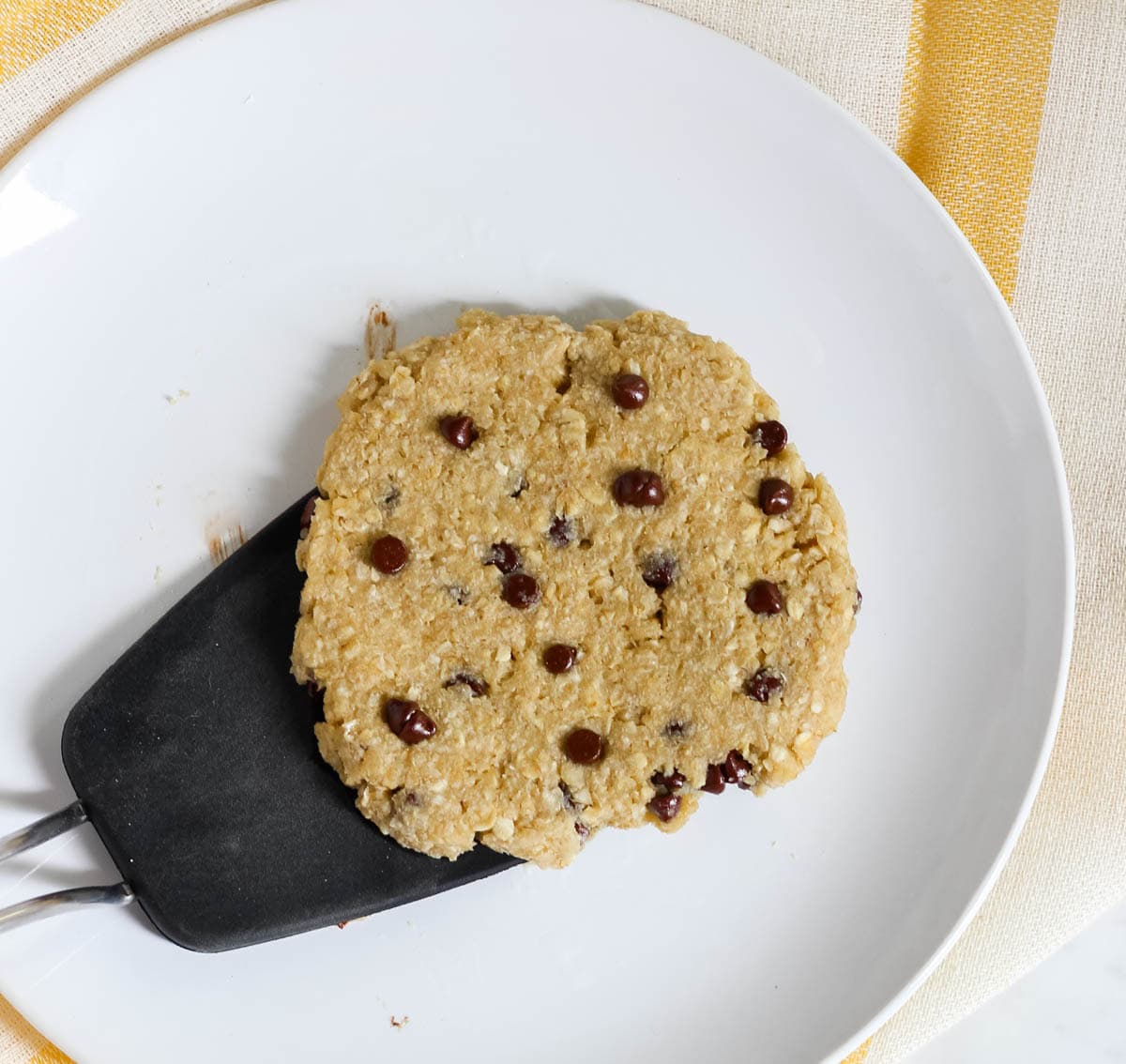 white plate with a black spatula picking up an oatmeal chocolate chip mug cookie.