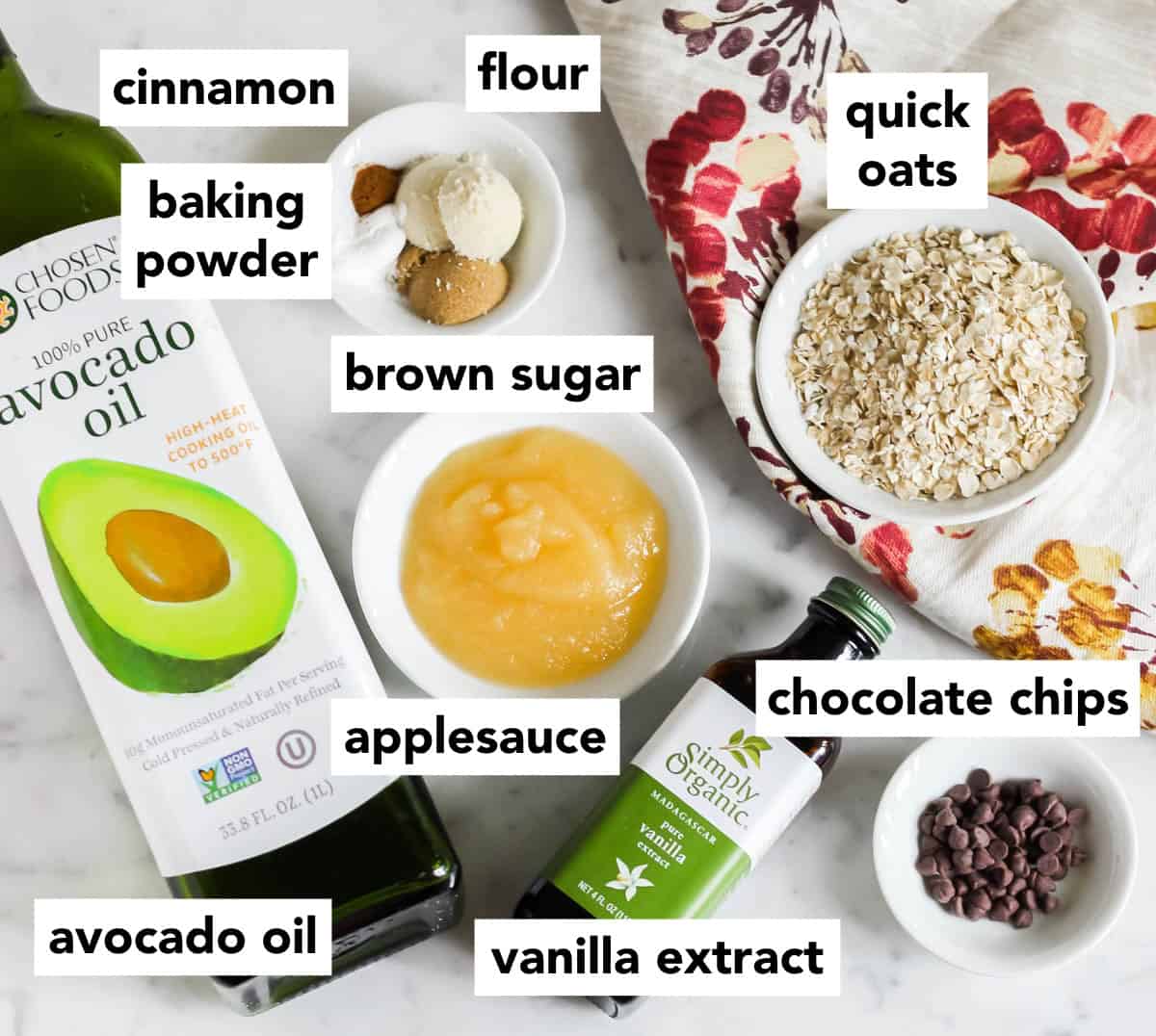 avocado oil, small bowls of applesauce, vanilla extract, oats, chocolate chips, and a small bowl of flour, brown sugar and cinnamon.